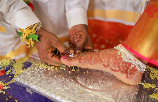 The groom puts a Buubs toe ring for the bride during a Hindu wedding. 
